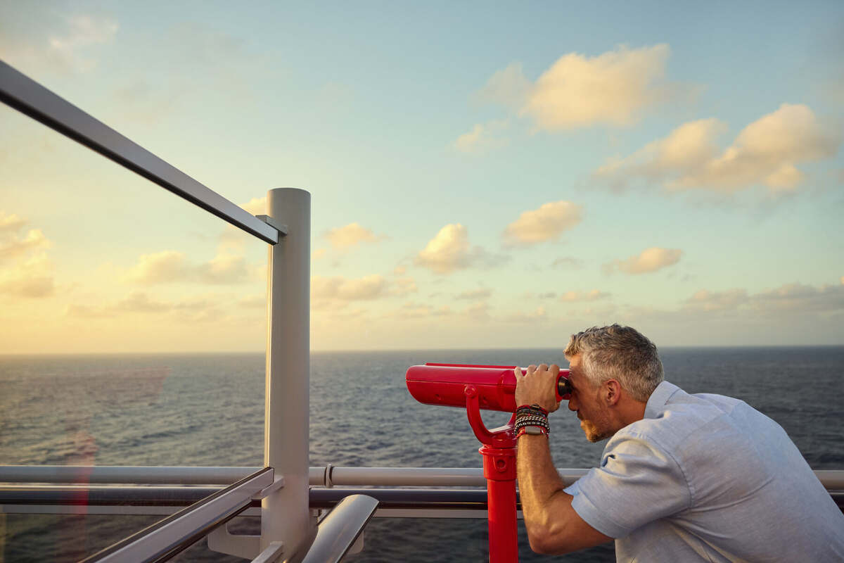 Guest watching the sunset through a deck telescope at sea